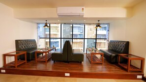 A spacious room with leather sofas, a central coffee table, and a large window offering a view of a residential building.