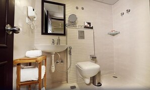 Un baño con inodoro, lavamanos y ducha. Hay un taburete de madera con toallas y un espejo sobre el lavamanos.