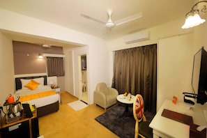 A hotel room with a bed, a desk, a chair, a TV, and a ceiling fan. - The Zinc By The Fern (Bengaluru)