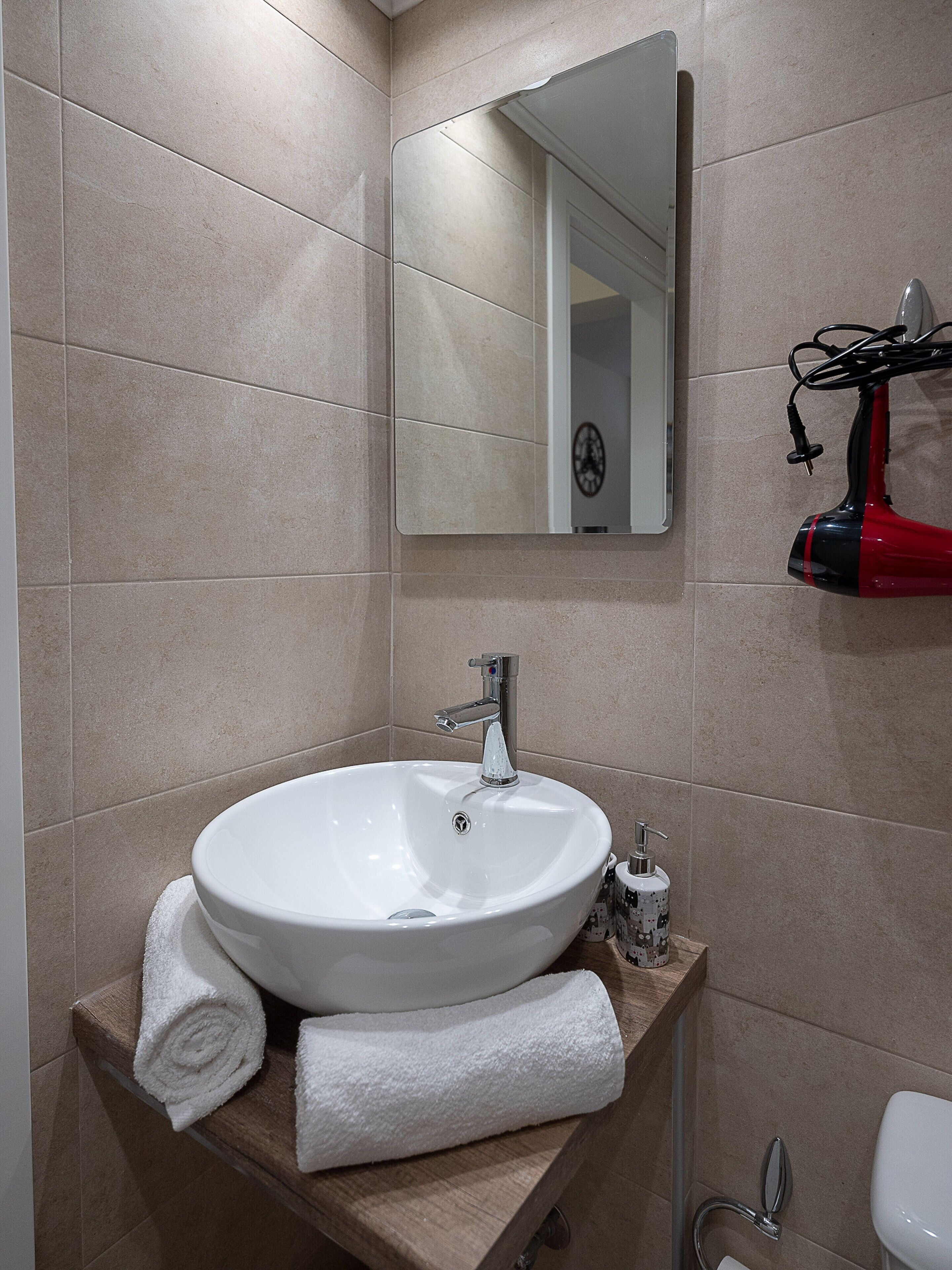 Een badkamer met een witte wasbak, een spiegel en een rode haardroger op een houten aanrecht.