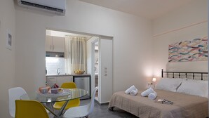 Habitación compacta con cama, mesa de comedor con sillas, kitchenette y baño visible a través de una puerta abierta.