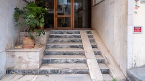 Una serie de escalones de mármol conducen a una puerta de cristal, con una planta en maceta a la izquierda y un cartel a la derecha.
