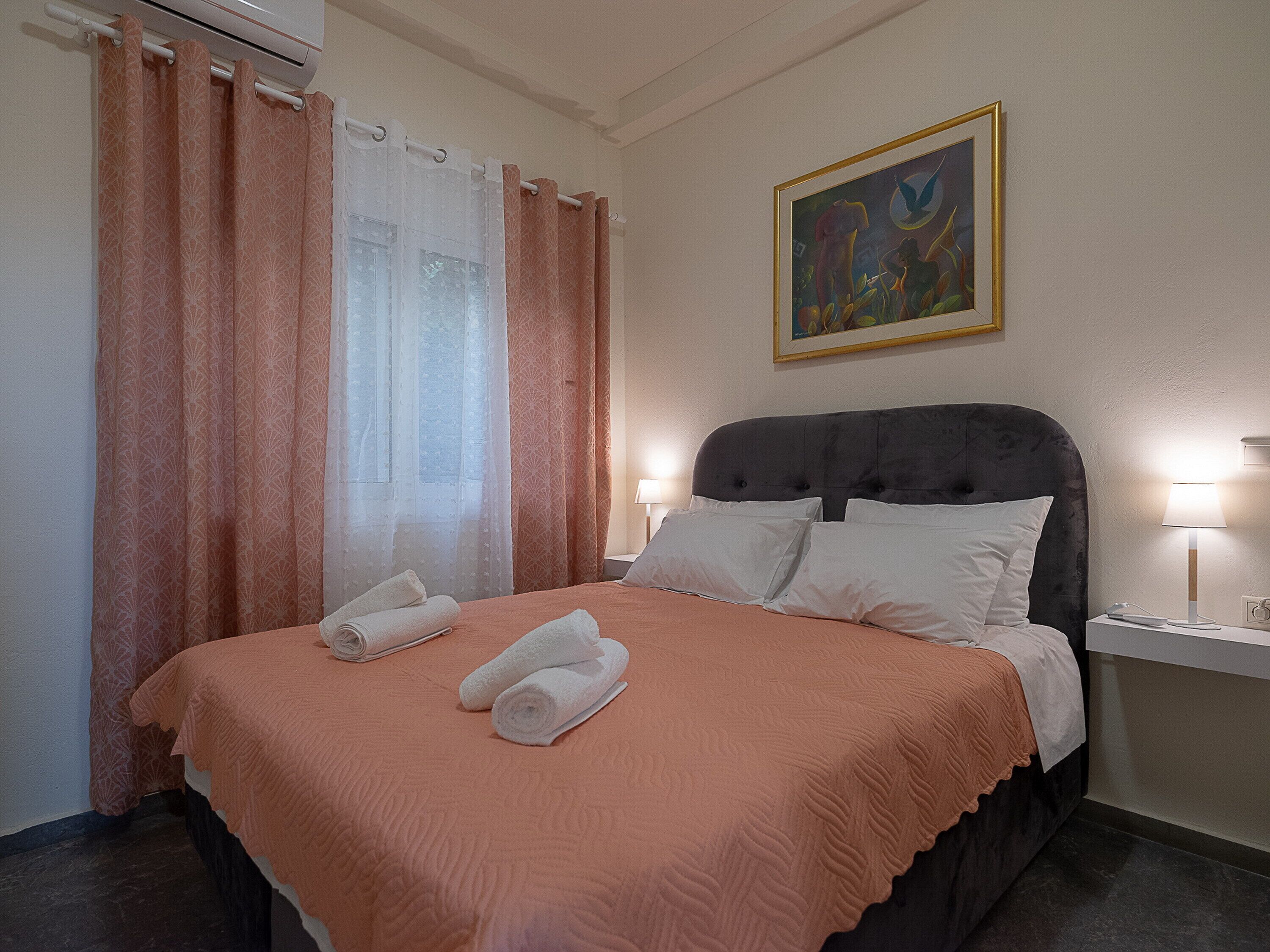 A neatly made bed with white pillows and towels, a dark headboard, and a painting on the wall.
