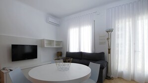 Una sala de estar moderna con una mesa redonda blanca, un sofá gris y un televisor de pantalla plana montado en la pared.