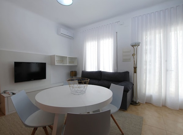 Un salon moderne avec une table ronde blanche, un canapé gris et un téléviseur à écran plat fixé au mur.