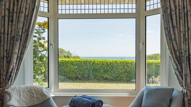 A room with two armchairs, a small ottoman, and a view of the sea through a bay window. - Downsview - large family home on the beach in Kingsdown (Deal)