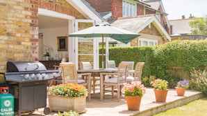 An outdoor patio with a grill, dining table, chairs, and potted plants. - Downsview - large family home on the beach in Kingsdown (Deal)