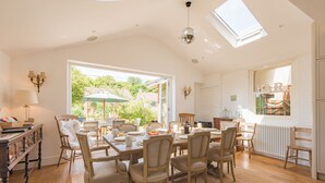 A spacious dining area with a high ceiling and skylight, wooden furniture, and a view of the outdoors. - Downsview - large family home on the beach in Kingsdown (Deal)