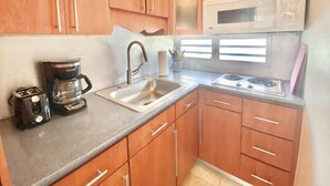A compact kitchen with wooden cabinets, a stainless steel sink, a microwave, a coffee maker, and a gas stove. - El Sol Beachfront + Pool + Beach + Parking (San Juan)