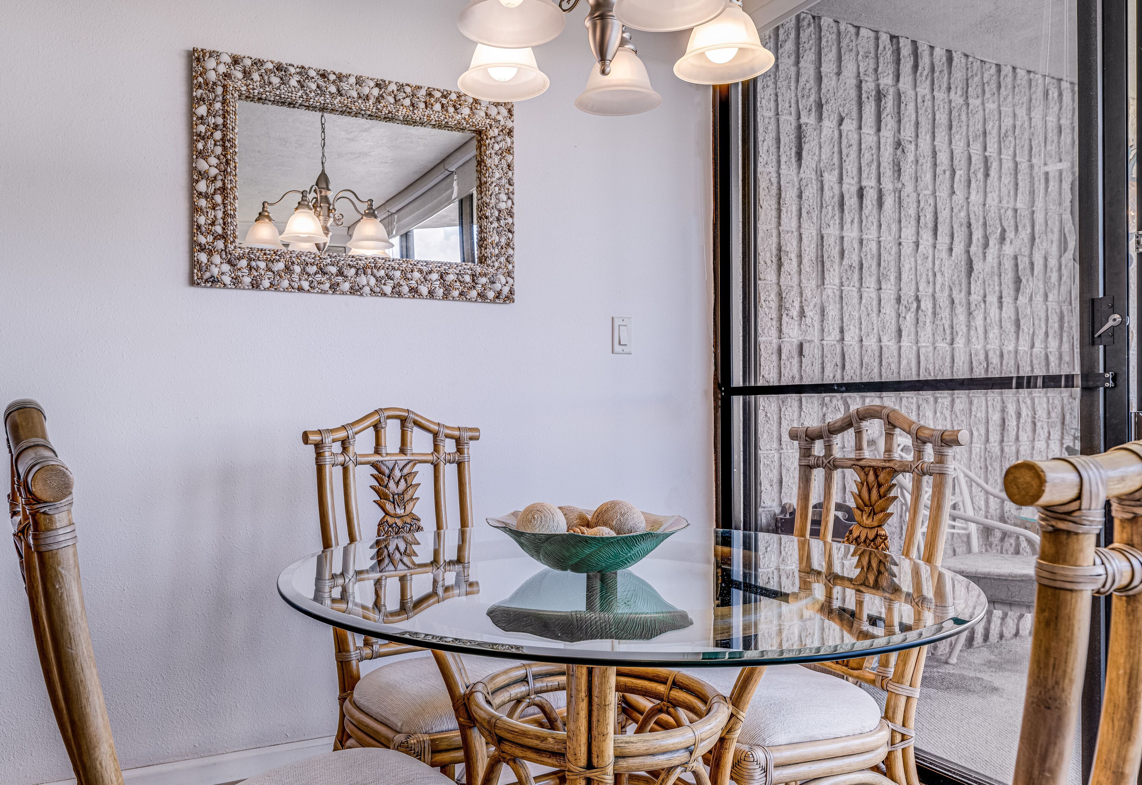 Un coin repas comprenant une table en verre, des chaises en osier, un miroir décoratif et un luminaire.