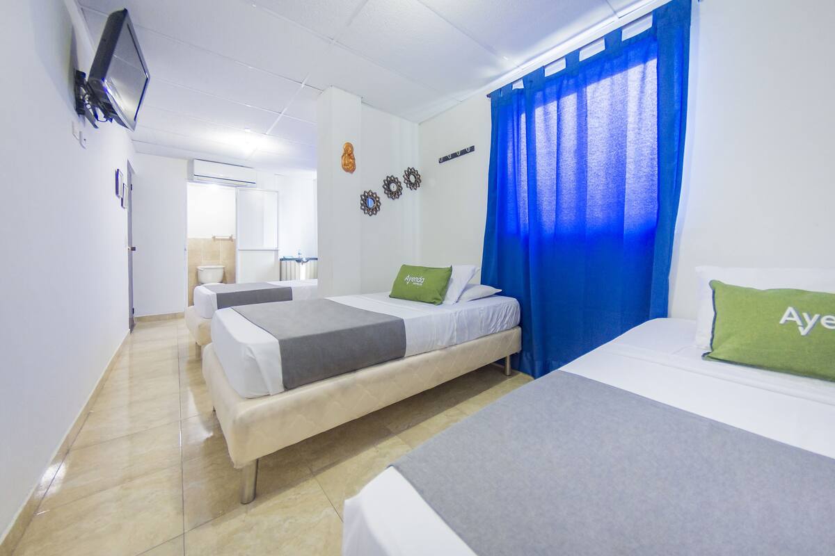 Habitación de hotel con dos camas, un televisor y un baño al fondo.