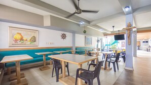 A restaurant with wooden tables and black chairs, a blue cushioned bench, and a crucifix on the wall. - Hotel Puerto Vigia (Cartagena)