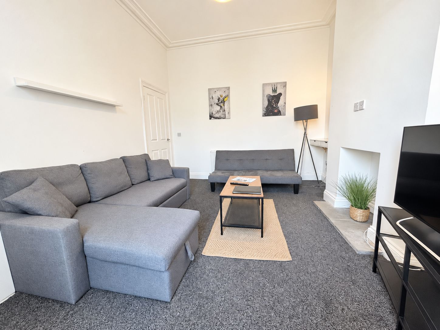 Ein modernes Wohnzimmer mit einem grauen Ecksofa, einem zusätzlichen Sofa, einem Couchtisch, einer Stehlampe und einem Fernseher.