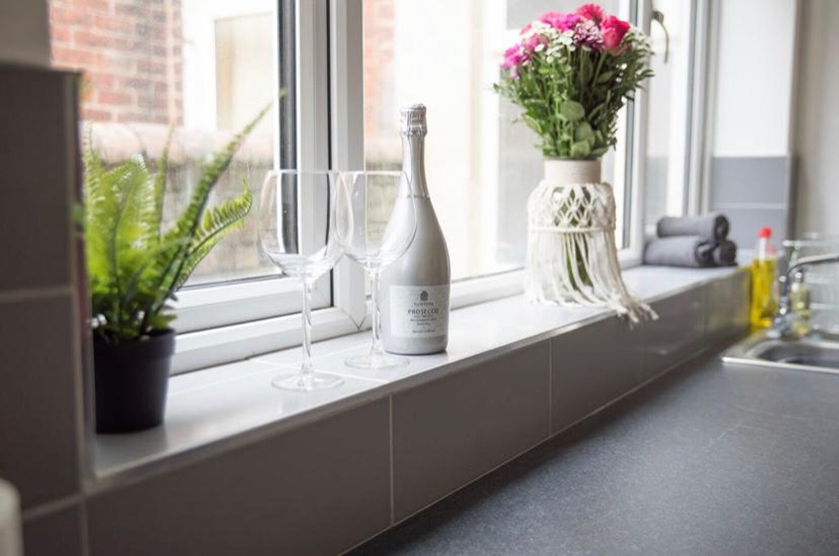 En køkkenbordplade med en vinflaske, to glas, en potteplante og en vase med blomster.