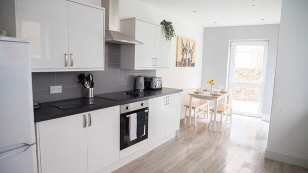 Une cuisine moderne avec des meubles blancs, un plan de travail noir et un coin repas comprenant une table et des chaises.