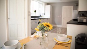 Un coin repas avec une table dressée pour deux personnes, agrémenté d’un vase avec des fleurs jaunes, de verres transparents et d’assiettes blanches.