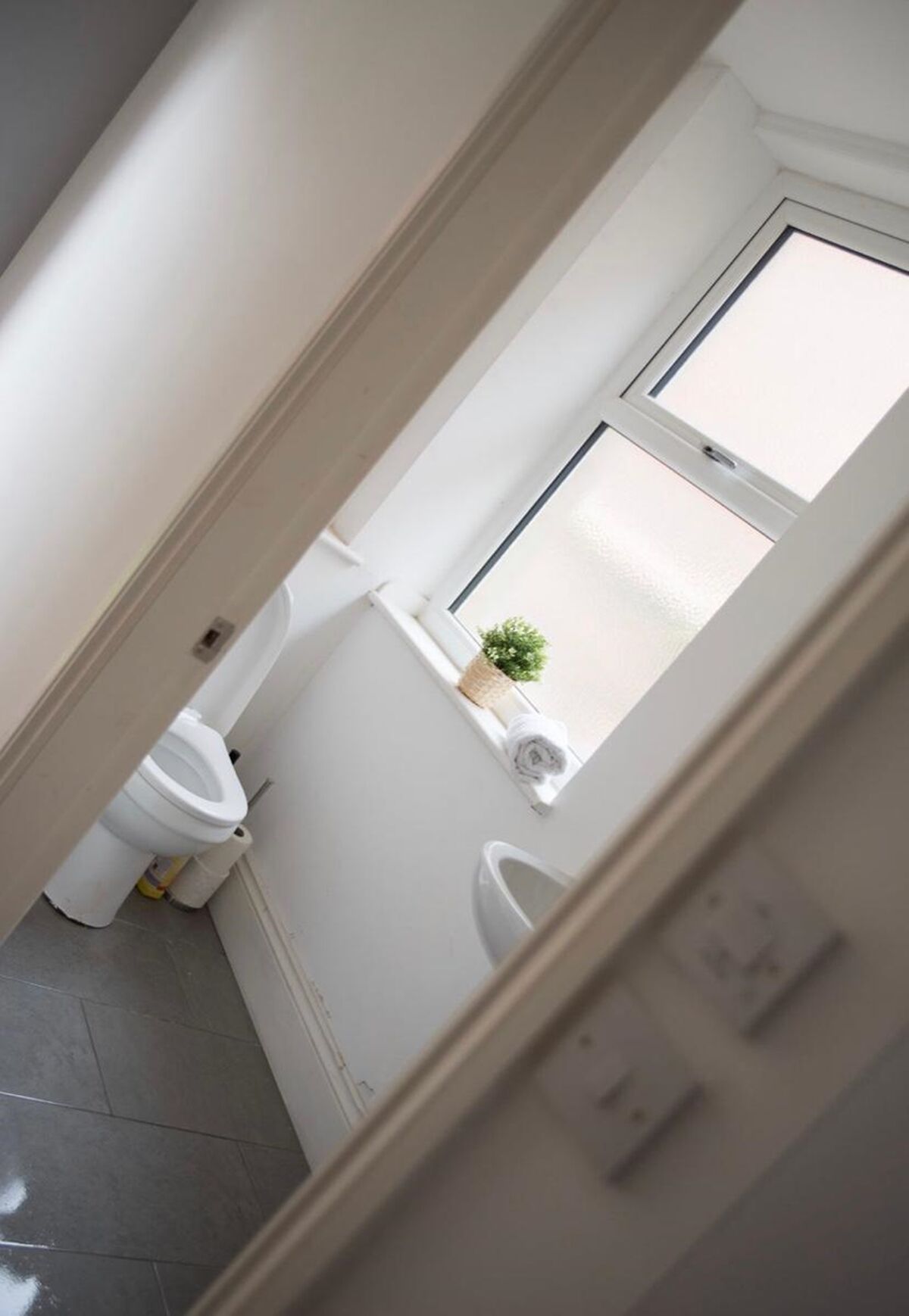 Un couloir étroit menant à une salle de bain équipée de toilettes, d’un bidet et d’une petite fenêtre.