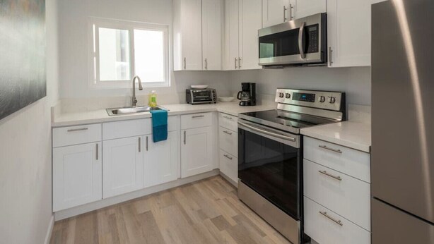 A modern kitchen with white cabinets, a stainless steel refrigerator, a microwave, a stove, and a sink. - Beautiful and Spacious 1 Bed, Steps to the Beach! (Marina del Rey)