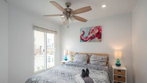 A bedroom with a large bed, a ceiling fan, a window, and a painting on the wall. - Beautiful and Spacious 1 Bed, Steps to the Beach! (Marina del Rey)