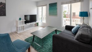 A modern living room with a flat-screen TV, a sofa, a coffee table, and a teal armchair. - Beautiful and Spacious 1 Bed, Steps to the Beach! (Marina del Rey)