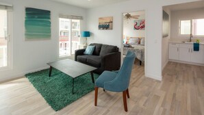 A modern living room with a sofa, a coffee table, and a chair. There is a green rug on the floor, and a window with blinds. - Beautiful and Spacious 1 Bed, Steps to the Beach! (Marina del Rey)