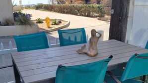 A wooden table with chairs, a decorative fish sculpture, and a view of a sandy area with plants and a yellow fire hydrant. - Beautiful and Spacious 1 Bed, Steps to the Beach! (Marina del Rey)