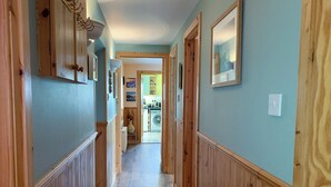A hallway with wooden paneling, a rug, and framed pictures on the walls. - Teeny’s Cottage is a spacious family holiday home set all on the ground floor. (Portree, near Dunvegan)