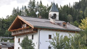 A traditional chalet with a steeply pitched roof, wooden balcony with flower boxes, and a small bell tower. - Alla Regia (Vodo Cadore)