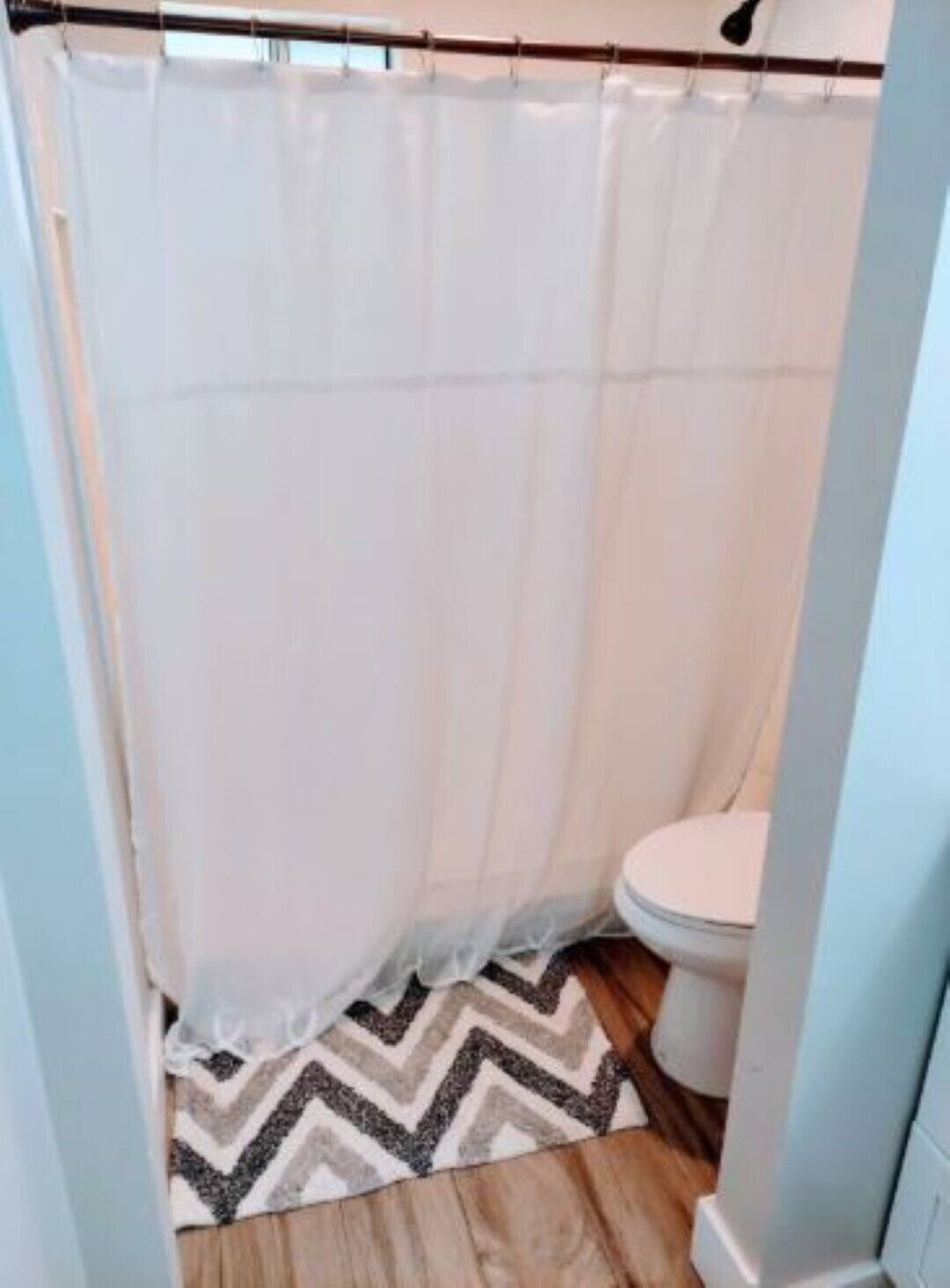 Une salle de bain avec un rideau de douche, des toilettes et un tapis à motifs.