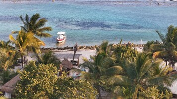 Vista de la playa con un barco amarrado cerca de la orilla, rodeado de palmeras y una estructura con techo de paja.