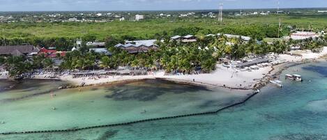 Vista aérea de un resort costero con zonas de playa, palmeras y aguas turquesas cristalinas.