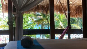 Una habitació amb un llit, una finestra i vista a palmeres sota un cel blau.
