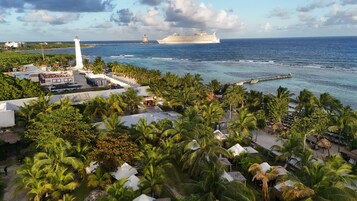 Un resort costero con un faro, un gran crucero y un muelle con barcos.