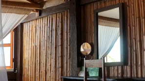 A room with bamboo panel walls, a wooden chair, a mirror, and a window with sheer curtains. - Blue Kay Eco Resort (Mahahual)
