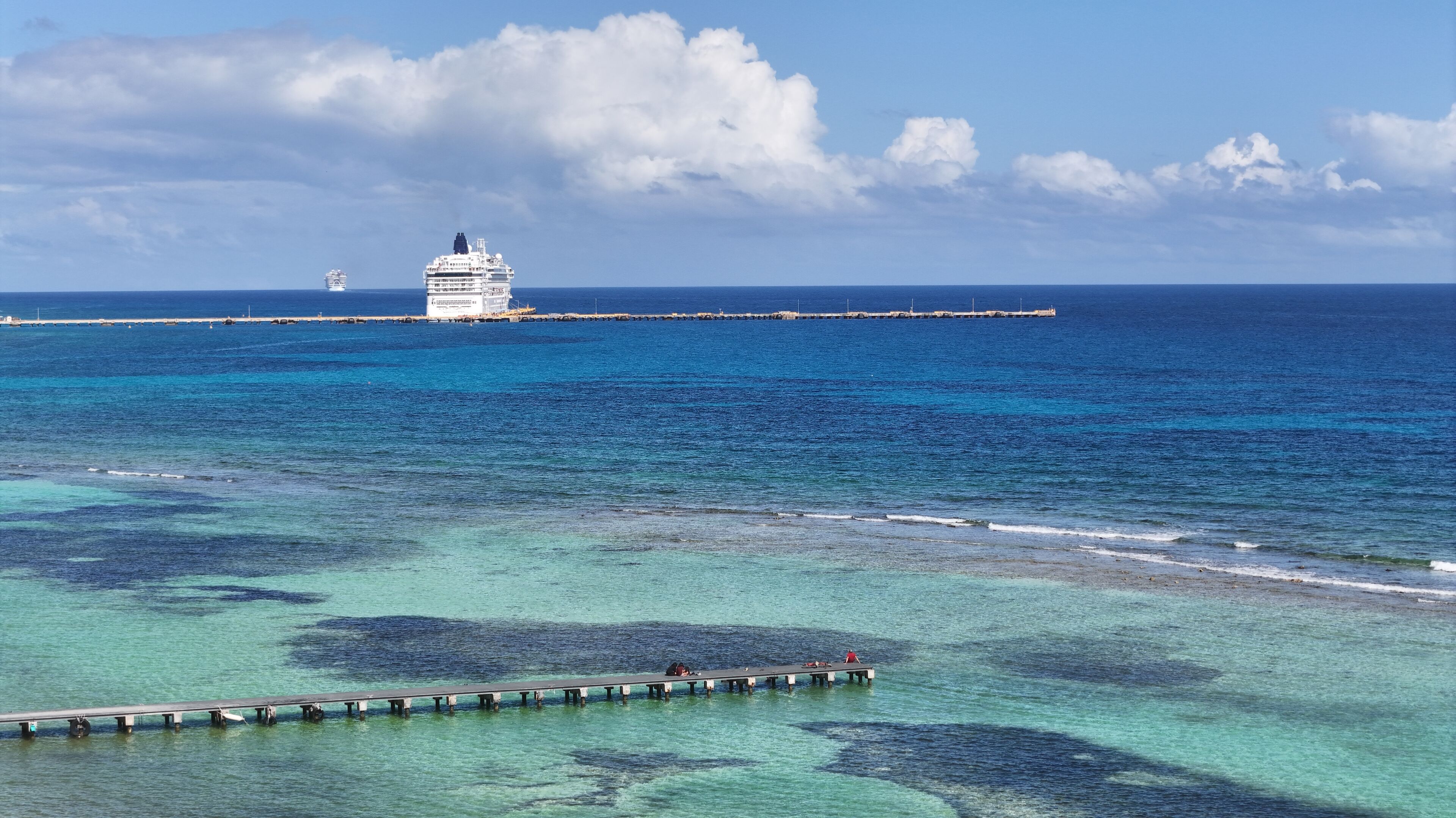 Un navire de croisière était amarré à un quai, bordant des eaux turquoise et limpides, et un ponton en bois s’étendait le long du rivage.