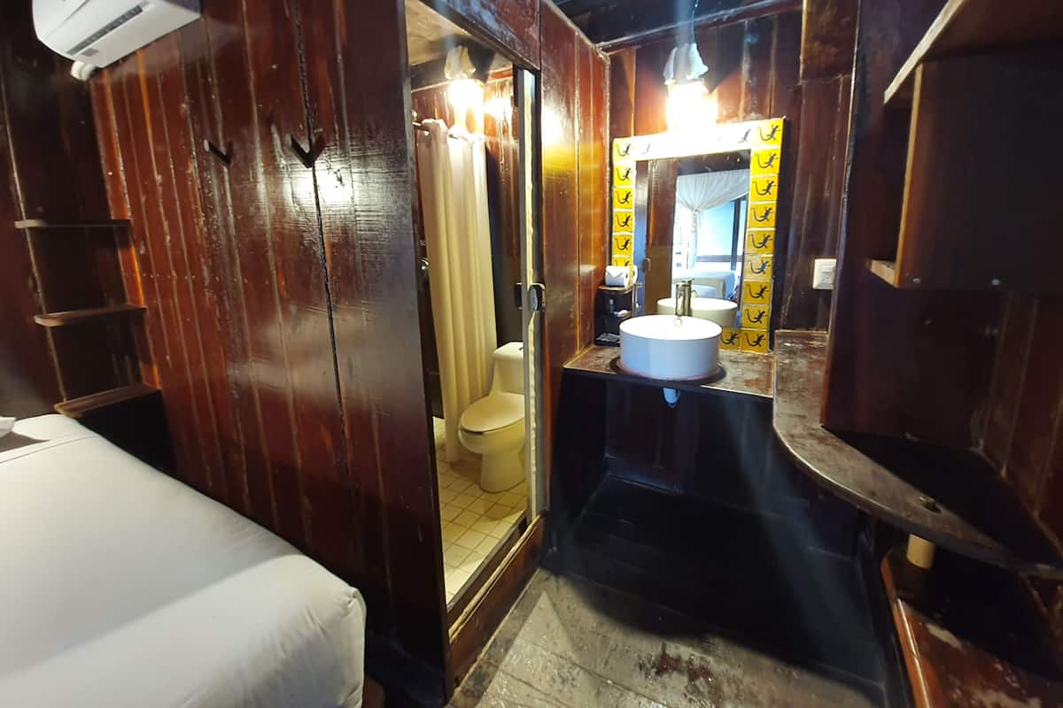 A compact, rustic bathroom with a wooden interior, a white sink, and a toilet visible through a glass door.