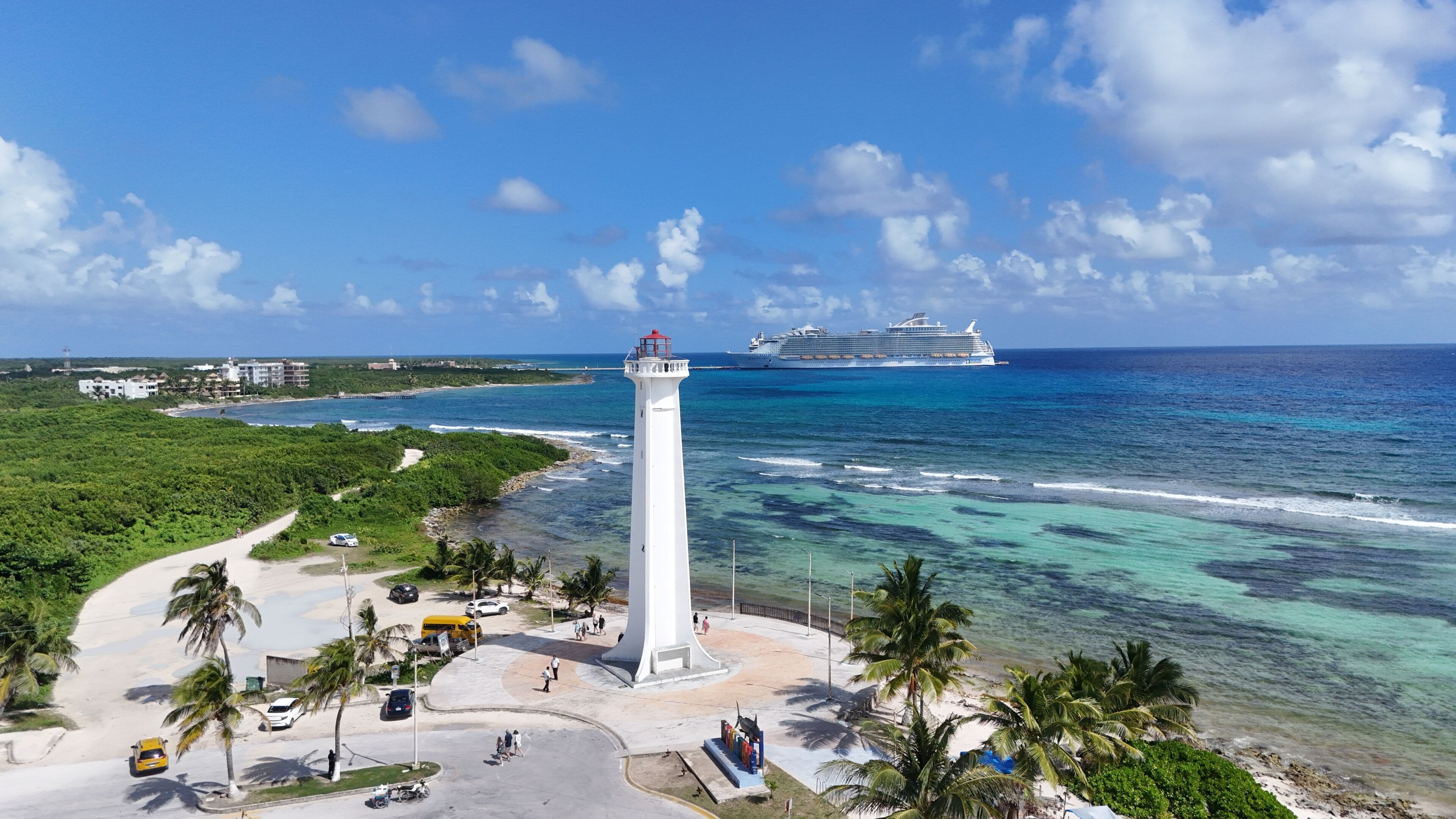 A coastal area with a lighthouse, a cruise ship, and a beach with palm trees.