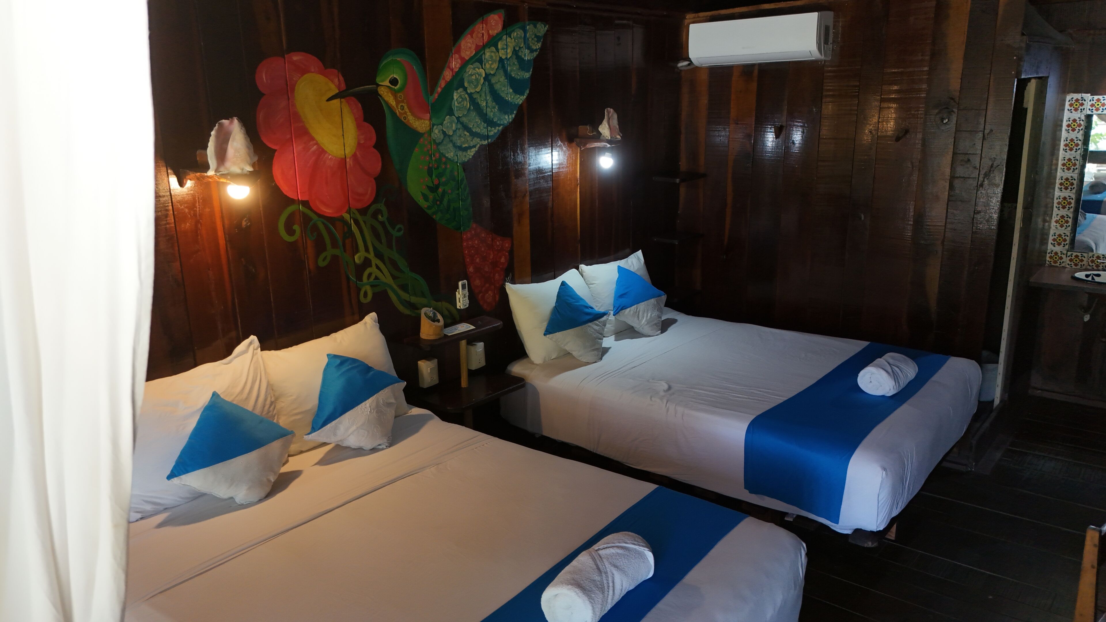 Dos camas individuales con ropa de cama azul y blanca, una pared de madera y un pájaro decorativo en la pared.