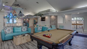 Ein geräumiges Wohnzimmer mit Billardtisch, zwei Sofas, einem Couchtisch und einem Deckenventilator.