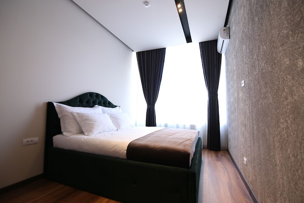 A modern hotel room with a bed, dark curtains, and a ceiling-mounted air conditioning unit.