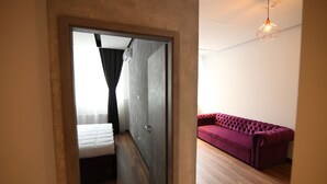 A modern room with a wooden floor, a red sofa, a bed with a white duvet, and a geometric pendant light. - Lunii 6 Apartments (Brasov)