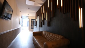 A modern hotel lobby with a leather sofa, a flat-screen TV mounted on the wall, and a decorative wall panel. - Lunii 6 Apartments (Brasov)