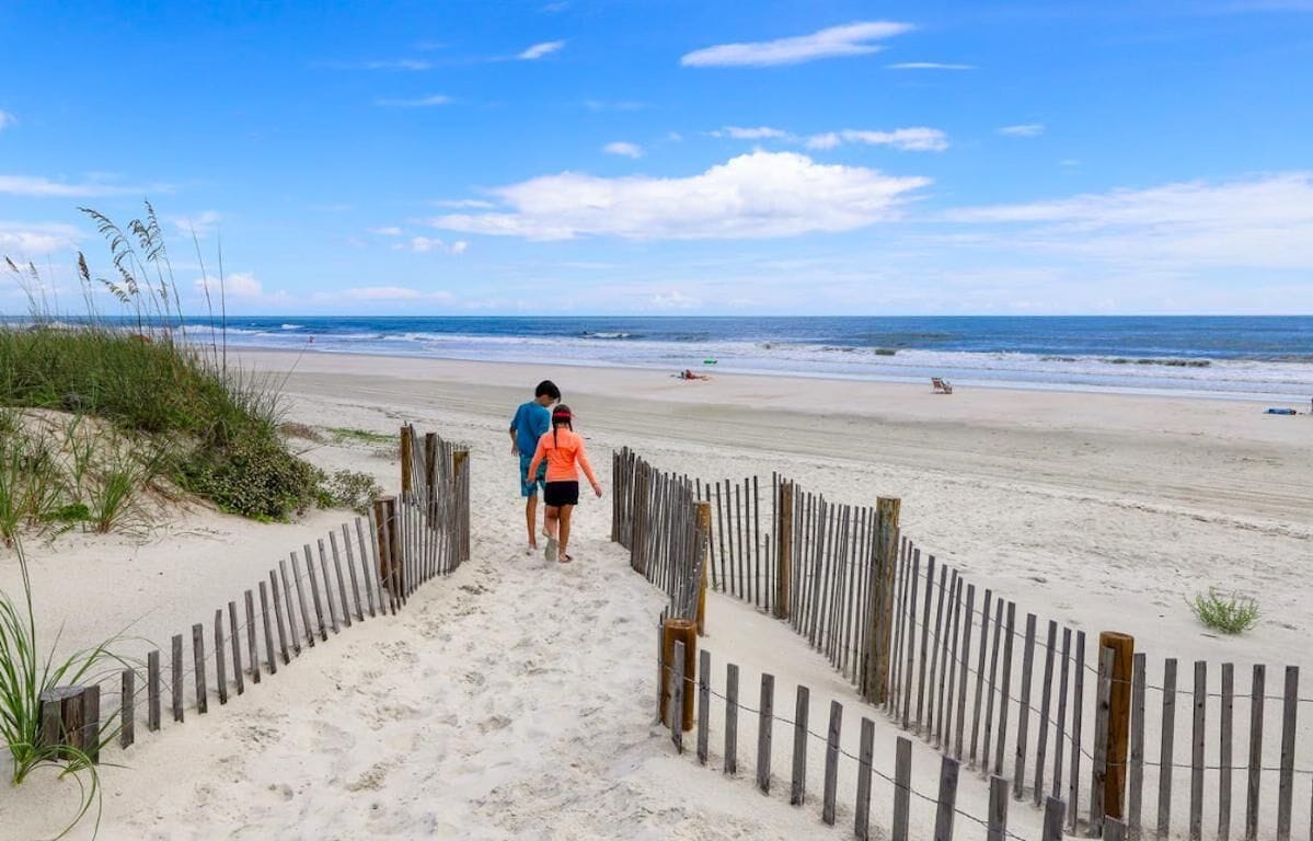 Ein sandiger Strand mit einer Holzlattenzaun, der zum Wasser führt.