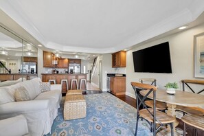 A modern living room with a sofa, a dining table, and a kitchen in the background.