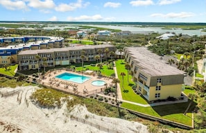 A hotel with multiple buildings, a central pool area, and a beach view.