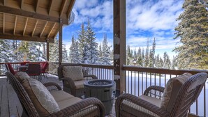 A covered outdoor seating area with wicker furniture and a fire pit, overlooking a snowy landscape with trees. - Cozy Brian Head Cabin Near Ski Resorts, Bike Trails, and National Forests (Brian Head)