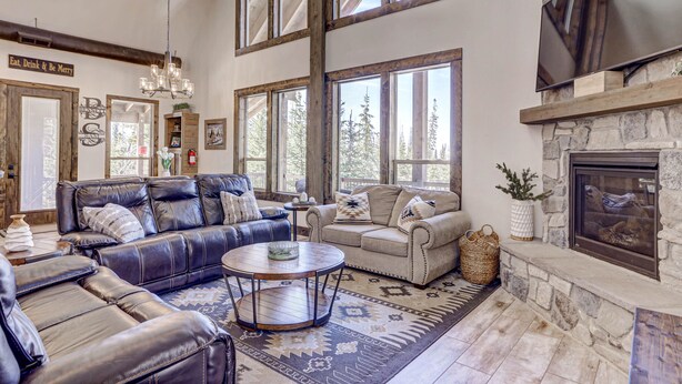 A spacious living room with leather sofas, a stone fireplace, large windows, and a chandelier. - Cozy Brian Head Cabin Near Ski Resorts, Bike Trails, and National Forests (Brian Head)