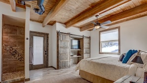 A bedroom with a large bed, wooden ceiling beams, a ceiling fan, and a stone fireplace. - Cozy Brian Head Cabin Near Ski Resorts, Bike Trails, and National Forests (Brian Head)