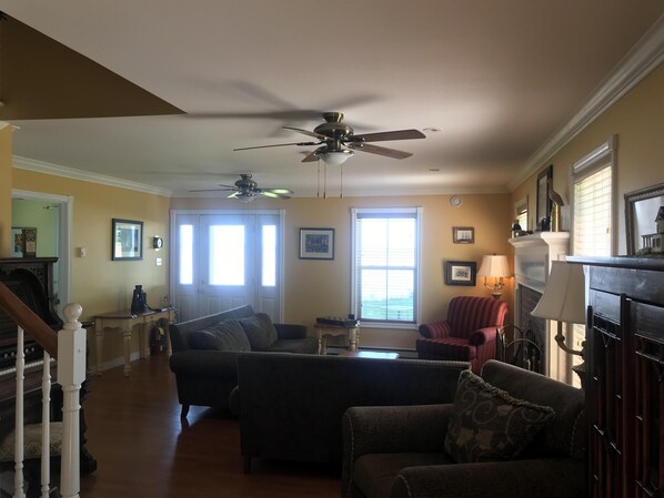 A living room with a ceiling fan, a fireplace, and a window with blinds. - Cresthaven By the Sea (Maitland)