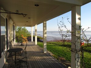 A covered porch with a view of the ocean, featuring a table, chairs, and a rocking chair. - Cresthaven By the Sea (Maitland)